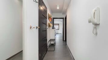 Un couloir avec un téléphone fixé au mur, une porte et un présentoir métallique.