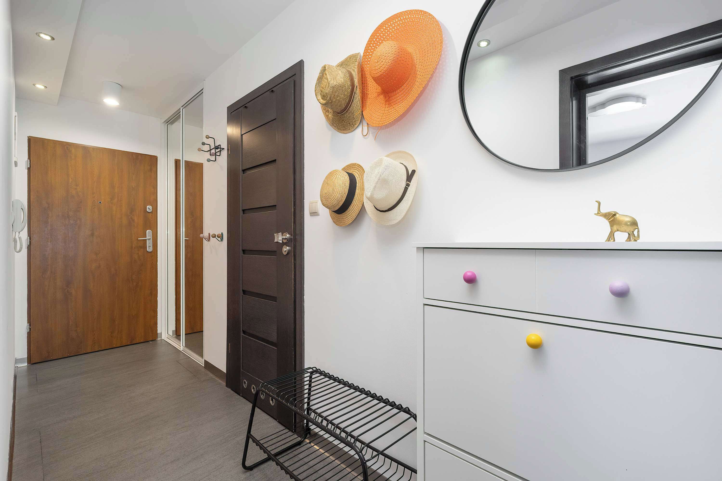 A hallway with a wooden door, a mirror, and a wall-mounted hat rack with several hats.