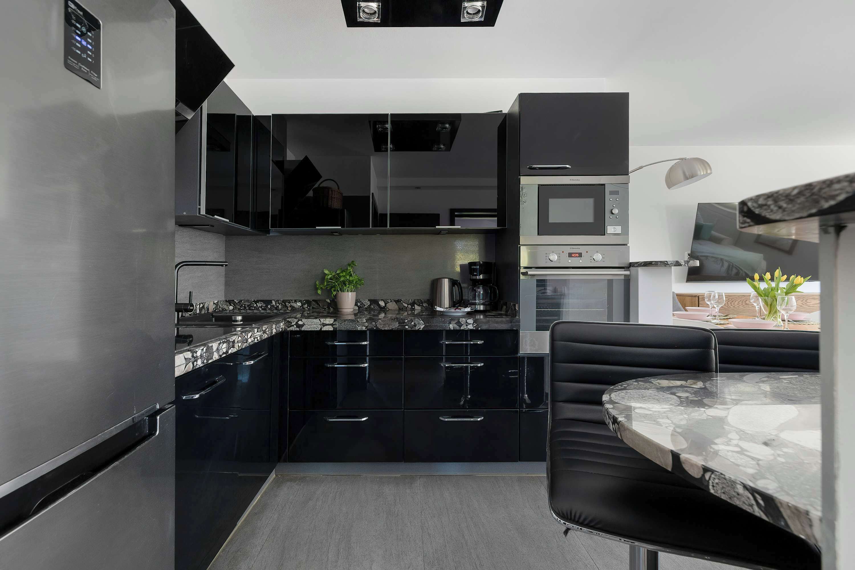 Une cuisine moderne avec des meubles noirs, un plan de travail en marbre, un four encastré et un coin repas comprenant une table en marbre et des chaises noires.