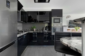 Eine moderne Küche mit schwarzen Schränken, einer Marmorarbeitsplatte, einem eingebauten Backofen und einem Essbereich mit einem Marmortisch und schwarzen Stühlen.