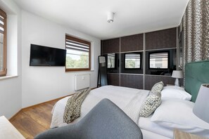 Ein modernes Schlafzimmer mit einem großen Bett, einem Flachbildfernseher, einem Spiegel und einem Fenster mit Jalousien.