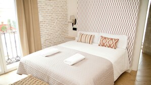 Ein Hotelzimmer mit Bett, einer Bank, einer Wand mit geometrischem Muster und einem Fenster mit Vorhängen.