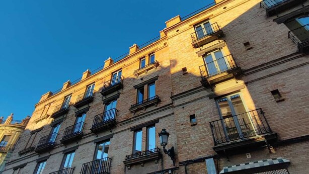 Ein mehrstöckiges Gebäude im traditionellen Baustil mit Balkonen, einem Eingang im Erdgeschoss mit einem Schild und einem strahlend blauen Himmel im Hintergrund.