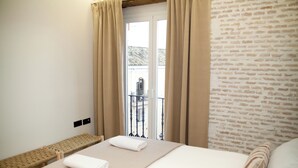 Ein Hotelzimmer mit Bett, einer Bank, einem Balkon mit Blick auf Gebäude und einer Backsteinmauer.