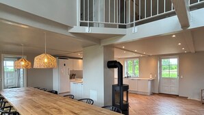 Een ruime keuken met een lange houten tafel, zwarte stoelen en een zwarte houtkachel.