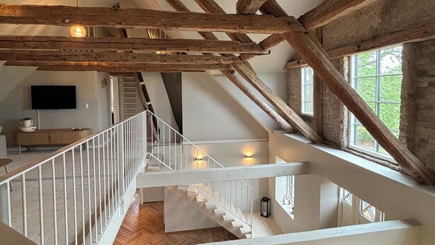 Een meerlaags interieur met zichtbare houten balken, een witte trap en een visgraatvloer.