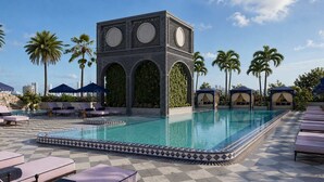 Un área de piscina con suelo de baldosas geométricas, sillas de descanso y un edificio decorativo con arcos.