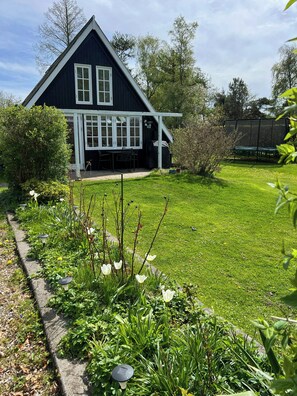 A house with a dark exterior, a covered porch, and a well-maintained garden with various plants and flowers. - Historic house with exposed beams near Hornbæk (Dronningmølle)