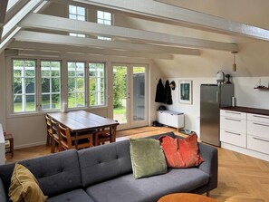 A spacious living area with a sofa, a dining table, and a kitchen area with a refrigerator and cabinets. - Historic house with exposed beams near Hornbæk (Dronningmølle)