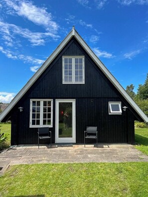 A black wooden house with a triangular roof, a front door, and two windows. - Historic house with exposed beams near Hornbæk (Dronningmølle)