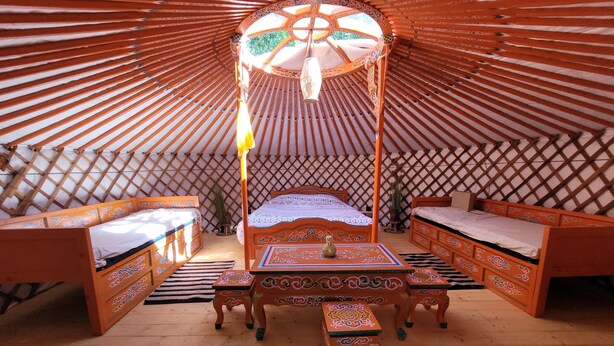 A yurt interior with a central bed, two sofas, a table, and a bench. - The Mongolian Yurt, an unusual accommodation (Souleuvre en Bocage)