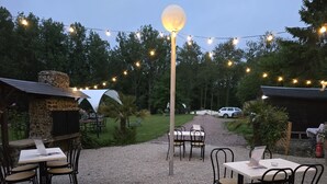 An outdoor patio with tables and chairs, string lights, a stone structure, and a gravel path. - The Mongolian Yurt, an unusual accommodation (Souleuvre en Bocage)