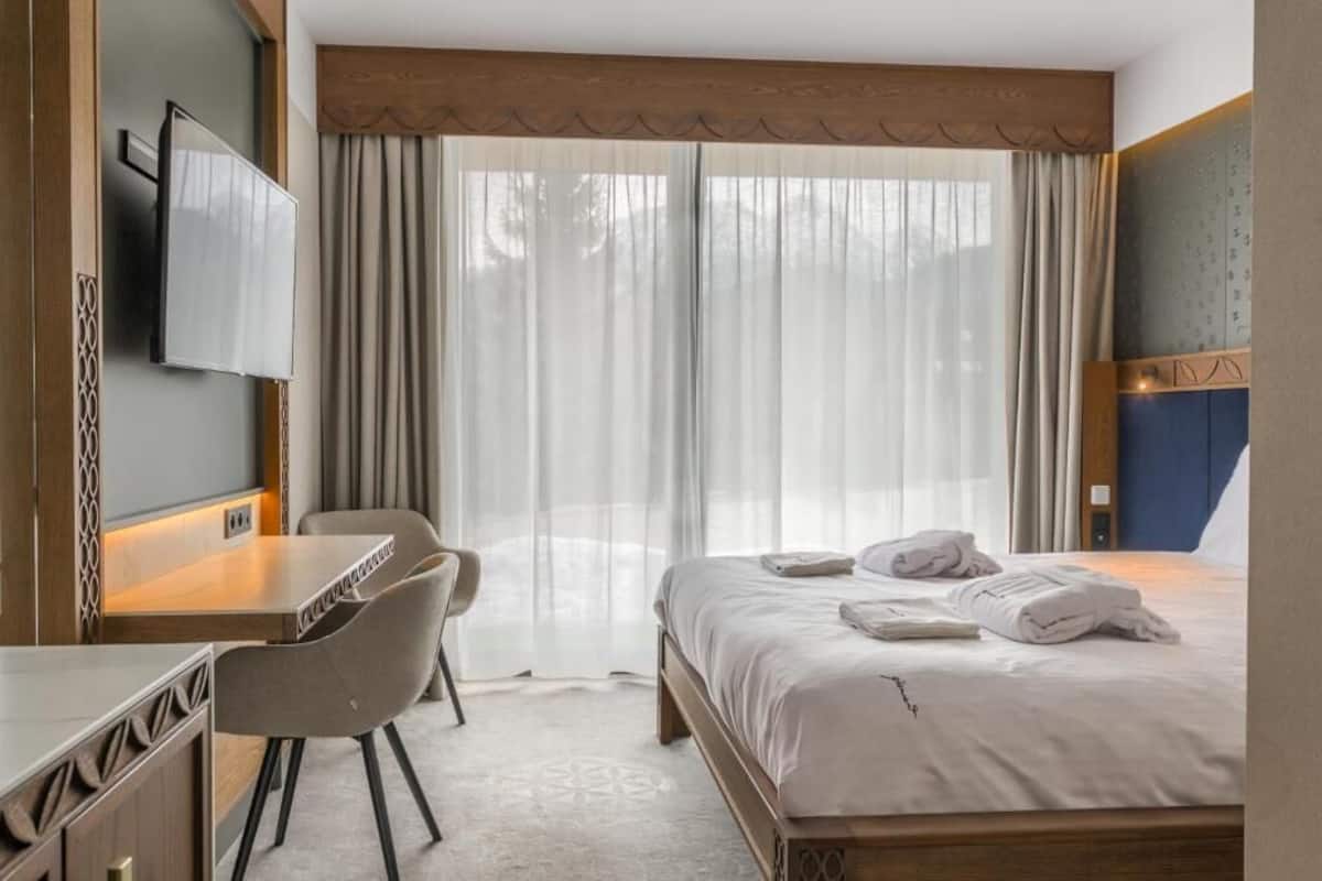 Une chambre d’hôtel avec un lit, un bureau, une chaise, une télévision et une grande fenêtre avec des rideaux.