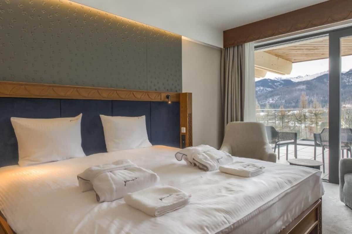 Une chambre d’hôtel avec un grand lit, une vue sur les montagnes et un balcon équipé de chaises.