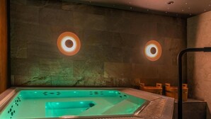 Un área de spa con jacuzzi, paredes de piedra y dos lámparas circulares.