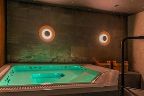 Een wellnessruimte met een bubbelbad, stenen muren en twee ronde lampen.