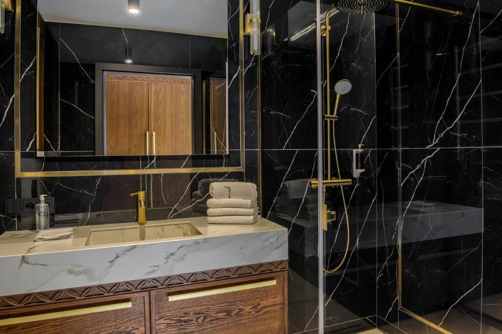 A modern bathroom with a marble vanity, a glass-enclosed shower, and a wooden cabinet.
