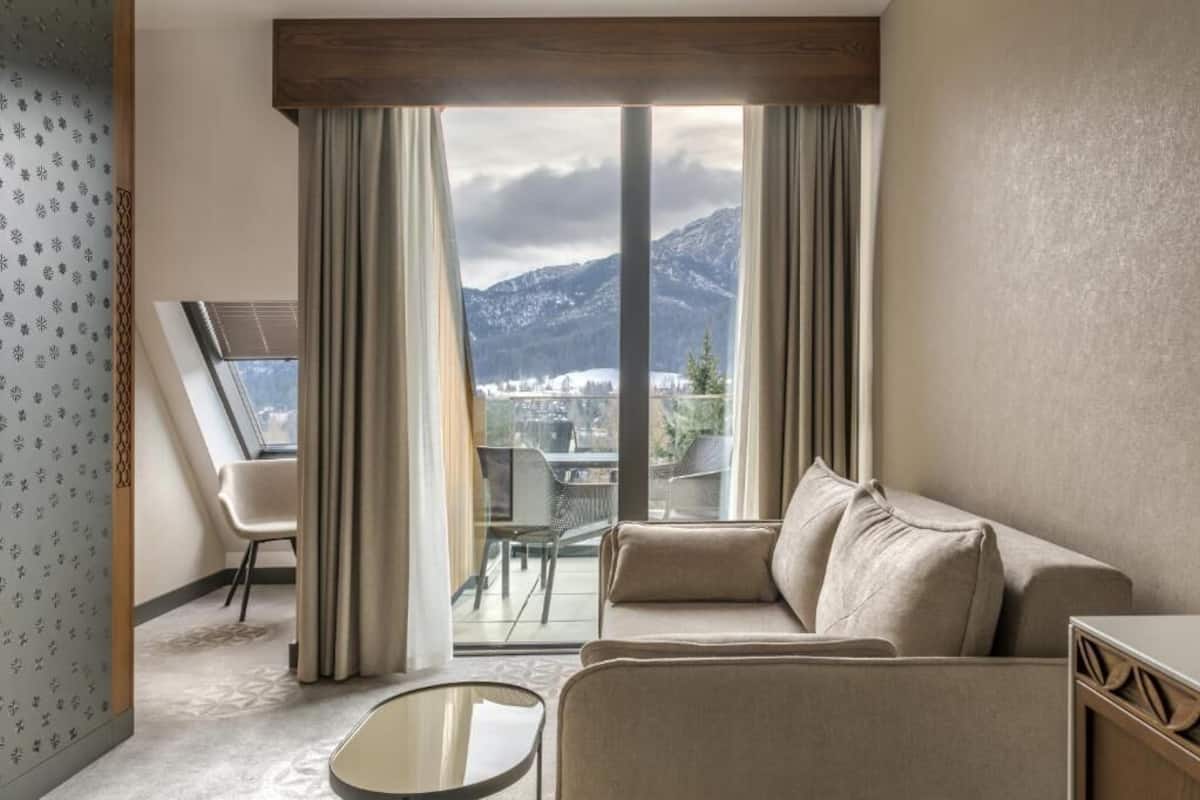 Une chambre d’hôtel moderne dotée d’une grande fenêtre, d’un canapé, d’une petite table et offrant une vue sur les montagnes.
