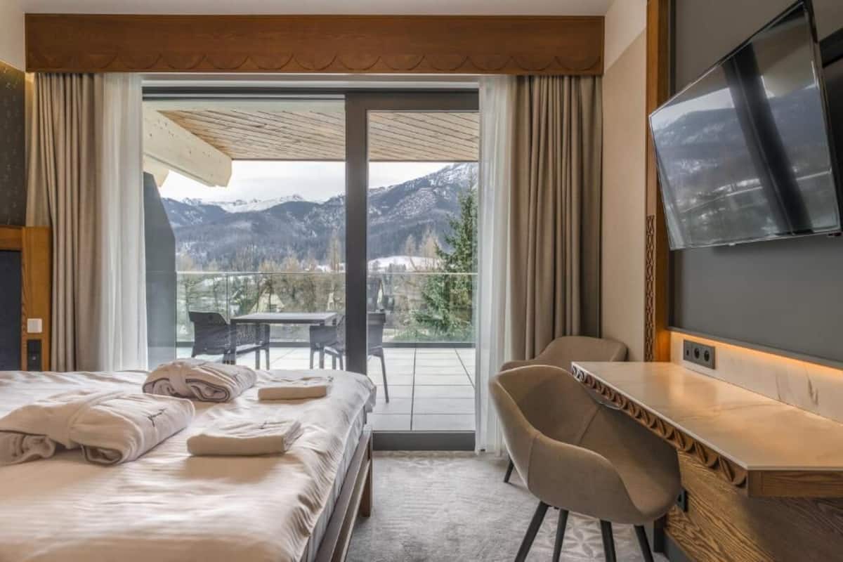 Une chambre d’hôtel équipée d’un lit, d’un bureau, d’une chaise, d’une télévision et d’un balcon avec vue sur la montagne.