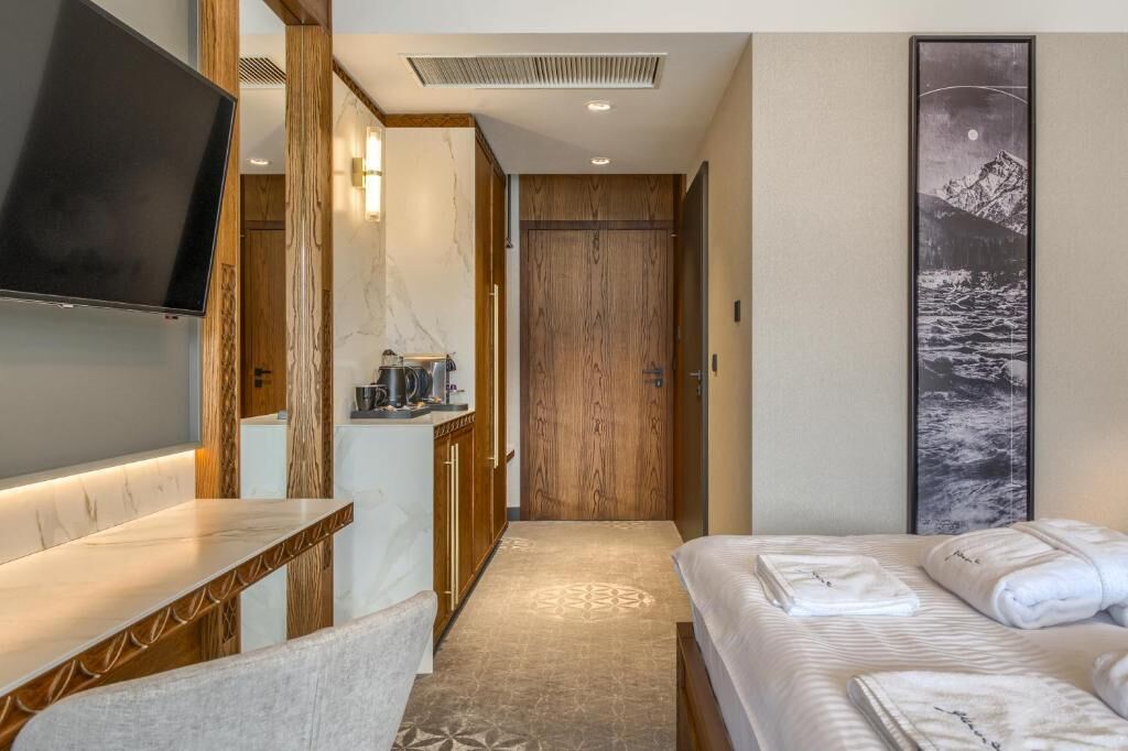 A hotel room with a bed, a TV, a wooden wardrobe, and a painting on the wall.