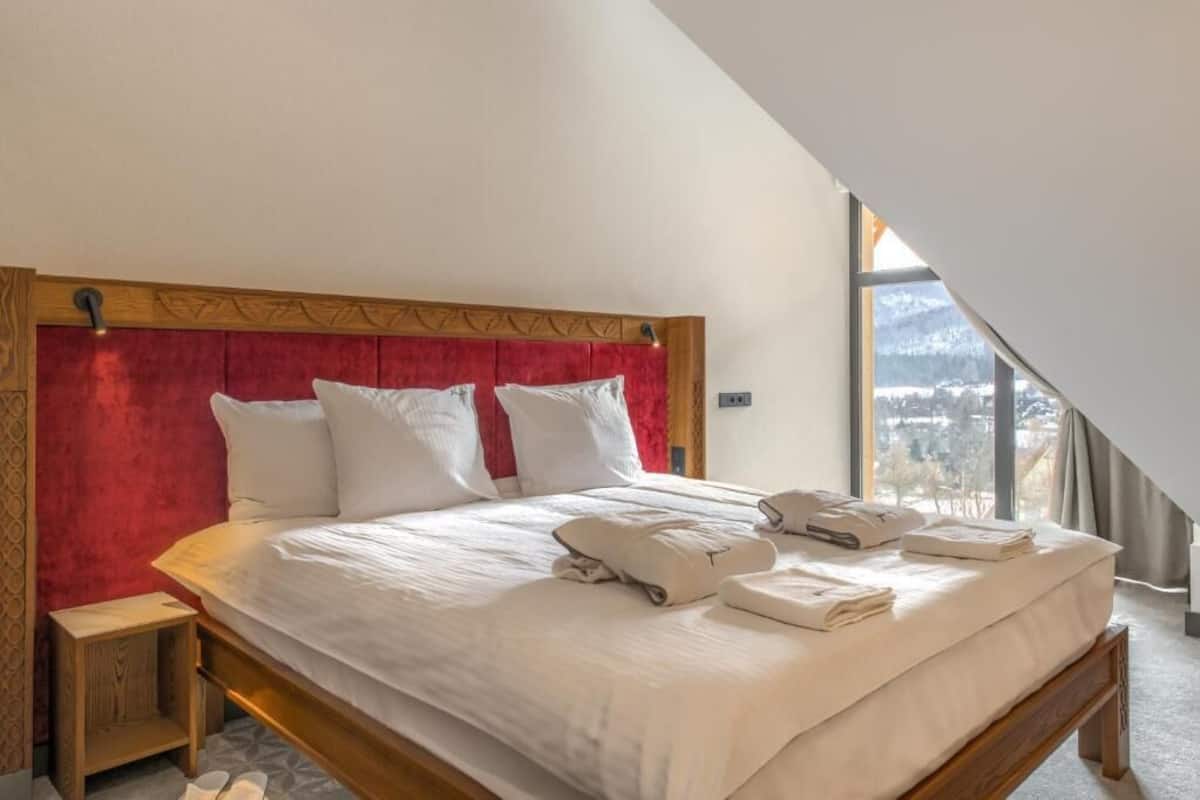 Une chambre d’hôtel avec un grand lit, une tête de lit en bois et une vue sur un paysage enneigé par une grande fenêtre.