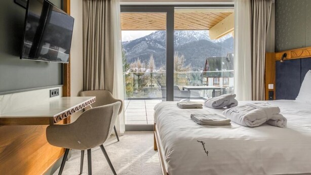 Habitación de hotel con cama, escritorio, silla, televisor y vistas a las montañas.