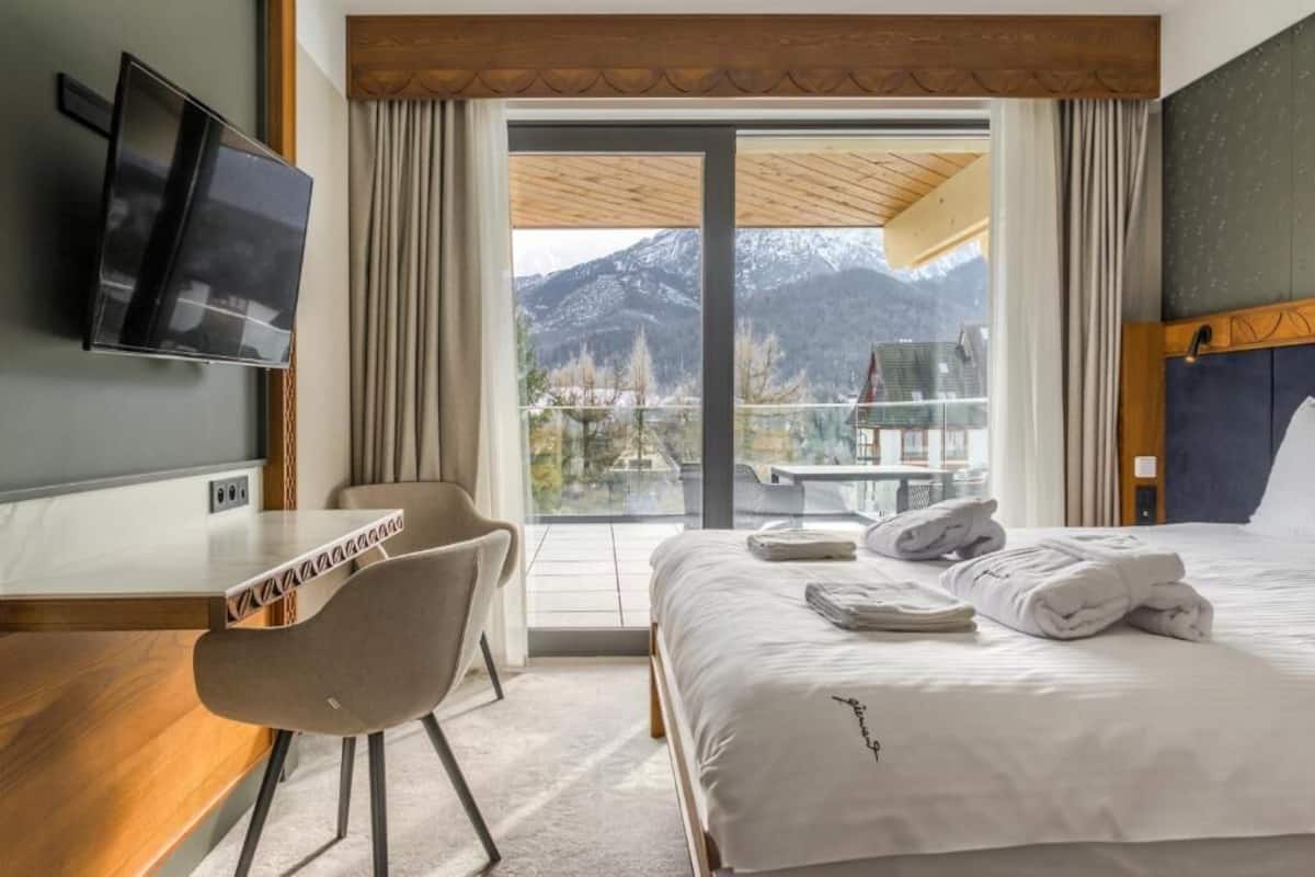 Une chambre d’hôtel équipée d’un lit, d’un bureau, d’une chaise, d’une télévision et offrant une vue sur les montagnes.