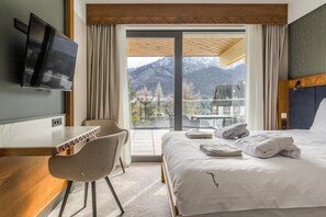 Ett hotellrum med en säng, ett skrivbord, en stol, en tv och utsikt över bergen.