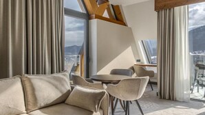 Una habitación de hotel moderna con sofá, sillas, una mesa y vistas a la ciudad a través de amplios ventanales.