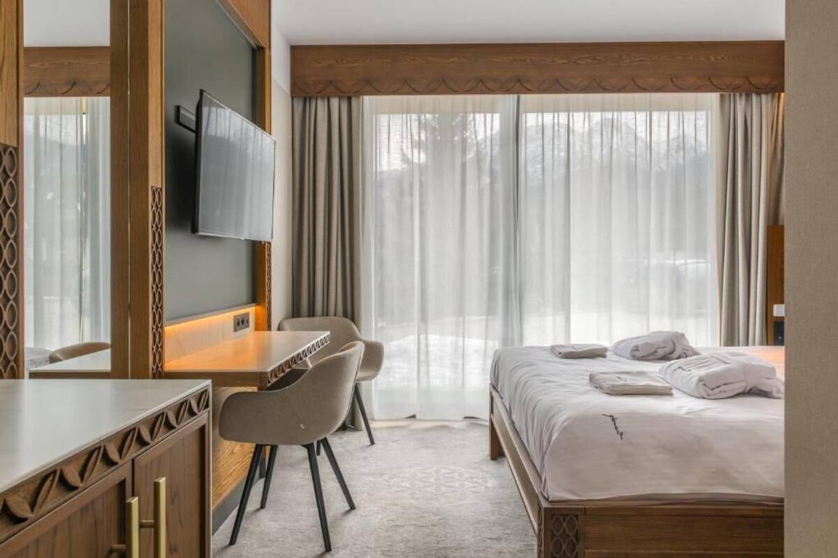 Une chambre d’hôtel équipée d’un lit, d’un bureau, d’une chaise, d’une télévision et d’une grande fenêtre avec des rideaux.
