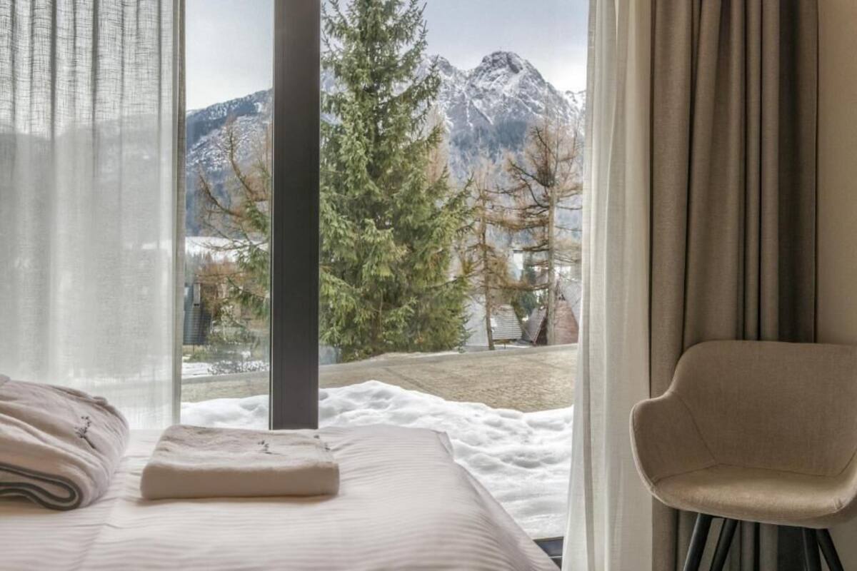 Une chambre à coucher avec un lit, une chaise, une fenêtre donnant sur les montagnes et les arbres.