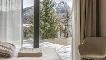 Un dormitorio con cama, una silla y ventana con vistas a montañas y árboles.