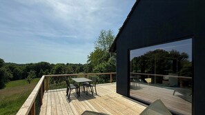 Un edificio moderno con una terraza de madera, una mesa y sillas, y un gran ventanal.
