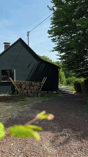 Ett hus med ett sluttande tak, ett fönster och en hög med vedträn.