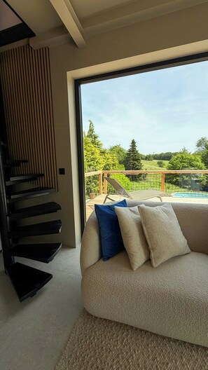Una sala moderna con un sofá, una escalera y vistas a una piscina y vegetación.