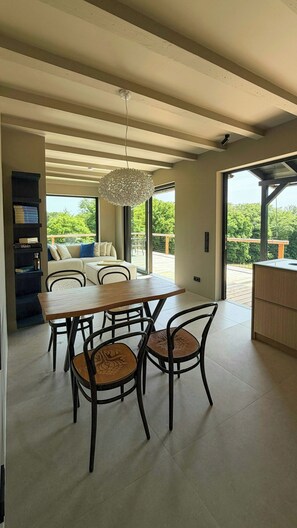 Un comedor moderno con una mesa y sillas de madera, una lámpara colgante y vistas a un balcón con follaje.