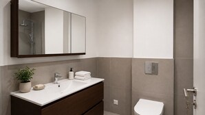 Un bany modern amb un mirall gran, un lavabo, un vàter i una dutxa.