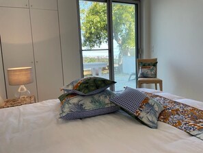 A bedroom with a bed, pillows, a lamp, a chair, and a view through a window. - Magnificent sea view villa (Vallauris)