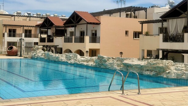 En swimmingpool med kristallklart blått vatten, omgiven av byggnader med balkonger och ett bergigt landskap.