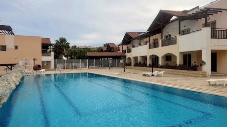 A swimming pool with lounge chairs and a covered area, surrounded by buildings with balconies and a stone wall.. Beautiful Stay Near the Beach Larnaca