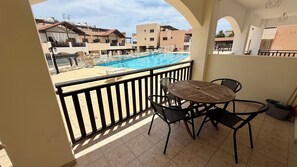 Un balcon donnant sur une piscine, une table avec des chaises et un sol carrelé.