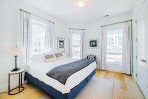 A bedroom with a bed, curtains, a lamp, and framed pictures on the wall.