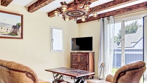 Ein Zimmer mit Holzboden, einer Kristallleuchtre, einem Fernseher, einer Kommode und zwei Ledersesseln.