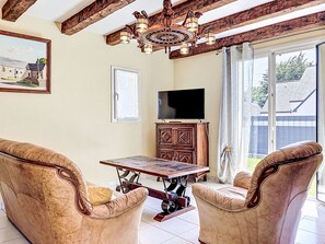 Ein Zimmer mit Holzboden, einer Kristallleuchtre, einem Fernseher, einer Kommode und zwei Ledersesseln.