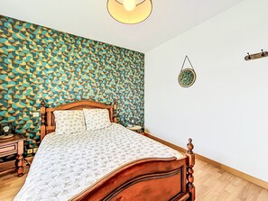Ein Schlafzimmer mit Wandmuster, einem hölzernen Bett, einem Nachttisch und einer Wandleuchte.