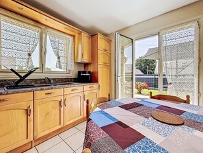 Una cocina con armarios de madera, cafetera y ventana con cortinas de encaje.