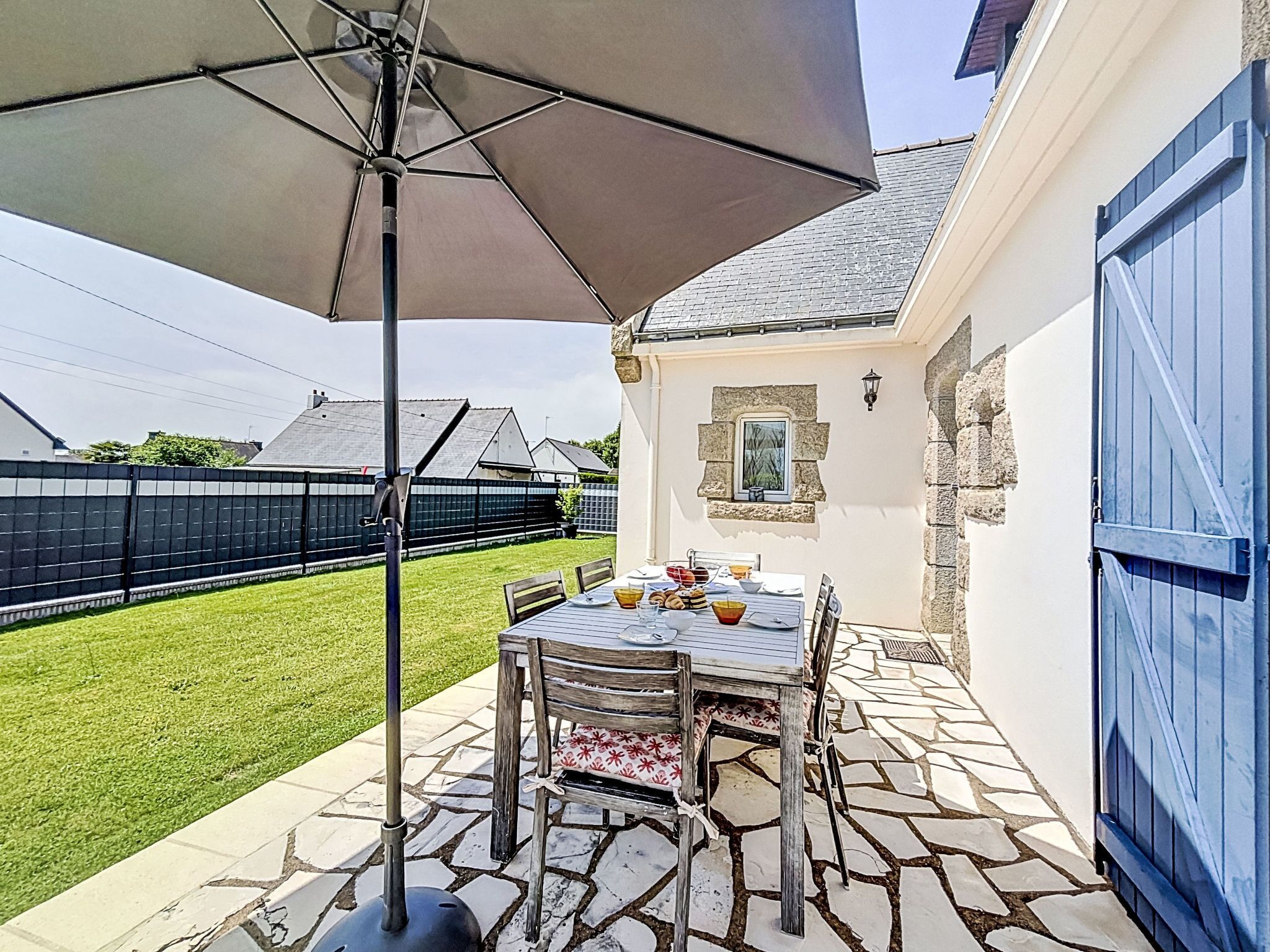Une terrasse extérieure avec une table, des chaises et un grand parasol.