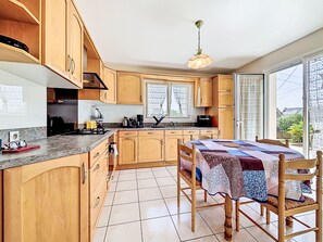 Una cocina con armarios de madera, una mesa de comedor con sillas, una ventana con cortinas de encaje y una lámpara colgante.