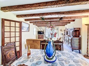 A dining area with a table set for two, a vase with flowers, wooden beams on the ceiling, and a view of the dining room. - Maison Le Guerno by Interhome (Le Guerno)