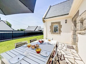 Ein Essbereich im Freien mit einem Tisch für vier Personen, umgeben von Steinmauern und einer überdachten Terrasse.